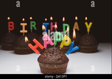 Alles Gute zum Geburtstag. Cupcakes mit brennenden Kerzen auf schwarzem Hintergrund, Nahaufnahme. Stockfoto