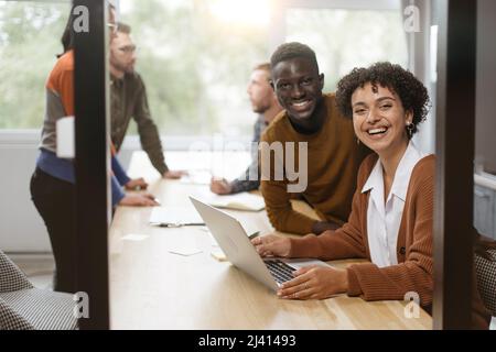 Die junge Frau und ihre Kollegin sitzen an einem Tisch in einem Coworking Stockfoto