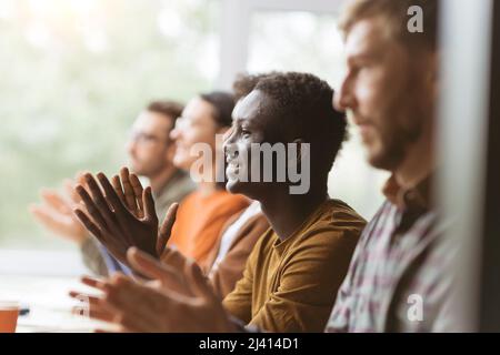 Eine Gruppe zufriedener Mitarbeiter applaudiert, während sie an derselben Ta sitzen Stockfoto