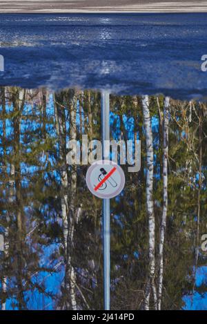 Eine verschwommene Reflexion in einer Pfütze. Ein Rauchverbotsschild an einer Tankstelle. Stockfoto