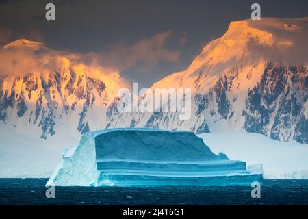 Am frühen Morgen fällt Licht auf einen Eisberg und Berggipfel, die den Gerlache-Kanal westlich der Danco-Insel, den Errera-Kanal, Antarktis, umgeben Stockfoto