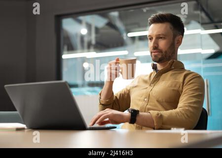 Geschäftsmann, Der Laptop Benutzt Und Kaffee Trinkt, Arbeitet Im Büro Stockfoto