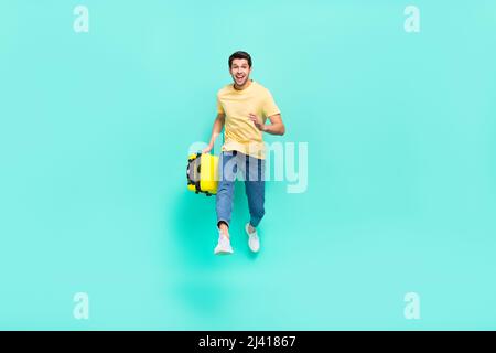 In voller Länge Foto von beeindruckt Brunet Kerl laufen mit Tasche tragen T-Shirt Jeans Sneakers isoliert auf blauem Hintergrund Stockfoto