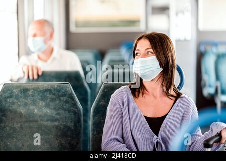 Positive Pendler mit Maske genießen ihre Zugfahrt Stockfoto