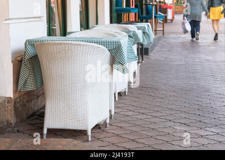 Im Sommer ist der Sitzbereich leer. Weiße Tische und Sessel auf der Außenterrasse des Sommercafés in der Straße. Restaurantbetrieb erwartet die Besucher. Stockfoto