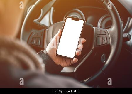 Mockup Smartphone leeren weißen Bildschirm in weibliche Fahrer Hand über Lenkrad, selektive Fokussierung Stockfoto