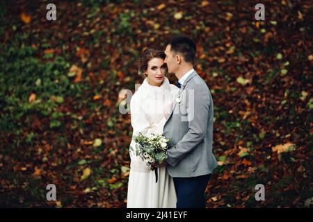 Bräutigam und Braut posieren im Herbstwald, zwischen Blättern. Stockfoto