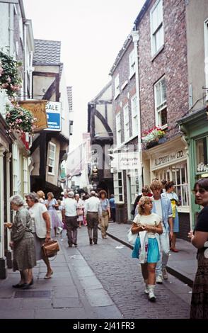 Menschen, die entlang der engen mittelalterlichen Fußgängerzone der Shambles im Stadtzentrum von York, Yorkshire, England, Großbritannien 1984 spazieren Stockfoto