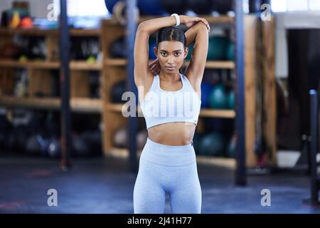 Ich tue das alles für mich. Porträt einer sportlichen jungen Frau, die beim Training im Fitnessstudio die Arme streckt. Stockfoto