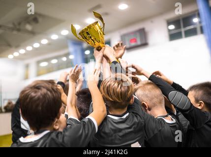 Schulsport-Teamkollegen, die sich nach dem Sieg im Hallensport eine goldene Trophäe sichern Stockfoto