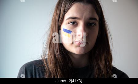 Ein ukrainisches Mädchen mit einer gemalten Flagge der Ukraine auf ihrem Gesicht. Stockfoto