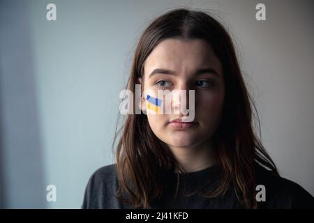 Ein ukrainisches Mädchen mit einer gemalten Flagge der Ukraine auf ihrem Gesicht. Stockfoto