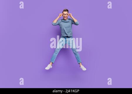 Foto von lustig aufgeregt Kerl tragen graue Hemd Arme Brille springen hoch isoliert violetten Hintergrund Stockfoto