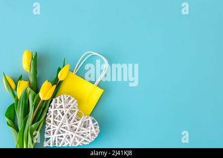 Flacher blauer Hintergrund mit Blumen und Papiertüten. Stockfoto