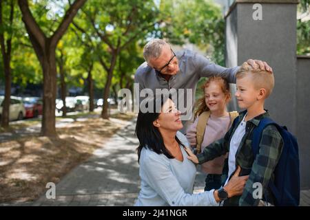 Glückliche Großeltern, die Enkel von der Schule nach Hause nehmen und draußen auf der Straße vor der Schule warten. Stockfoto