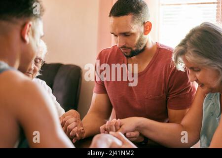 Die Familie, die zusammen betet, bleibt zusammen. Aufnahme einer Familie, die die Hände mit geschlossenen Augen im Gebet hält. Stockfoto