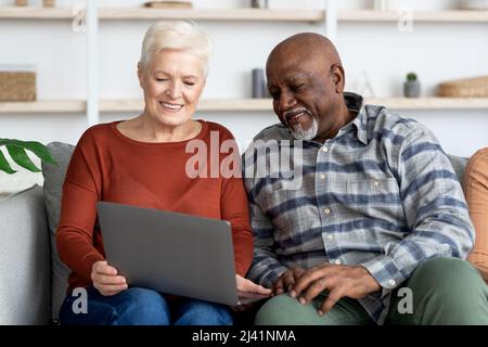 Glückliche ältere Dame, die Fotos ihrer Freundin auf dem Laptop zeigt Stockfoto