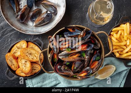 Belgische Muscheln mit Pommes frites und geröstetem Brot, mit Weißwein, darüber flach auf schwarzem Hintergrund geschossen Stockfoto