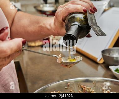 Der Koch gießt Olivenöl aus der Flasche in ein Gericht mit Lachs Stockfoto