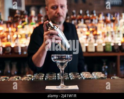 Der Barkeeper macht einen Cocktail mit einem Shaker hinter der Theke im Pub Stockfoto