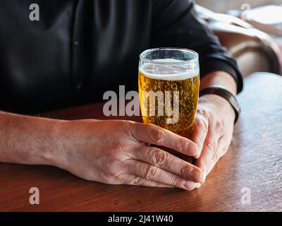 Hände eines Mannes, der ein Glas Bier auf der Bar oder dem Pub hält. Stockfoto