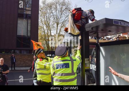 London, Großbritannien. 10.. April 2022. Die Polizei verhindert, dass ein Protestler auf eine Telefonzelle klettert. Die Demonstranten der Extinction Rebellion setzen ihre jüngste tägliche Kampagne fort, die voraussichtlich mehr als eine Woche andauern wird, und fordern die Regierung auf, fossile Brennstoffe zu beenden und gegen den Klimawandel zu handeln. Stockfoto