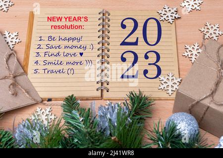 2023 Neujahrsvorsatz - Hand hält einen Stift und schreibt Pläne für das neue Jahr auf: Glücklich sein, Liebe finden, Geld sparen, lächeln, auf dem Tisch reisen w Stockfoto