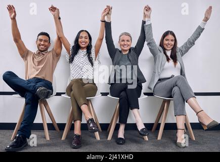Wir haben tolle Arbeit geleistet. Aufnahme einer Gruppe von Geschäftsleuten, die sich mit erhobenen Armen hinsetzen. Stockfoto