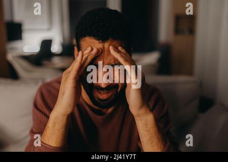 Porträt des deprimierten jungen Afrikaners - amerikanischer Mann mit Kopf in den Händen, der zu Hause sitzt. Stockfoto