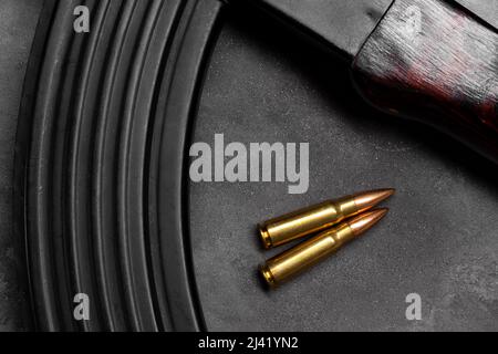 Zwei Kugeln und Kalaschnikow-Sturmgewehr auf grauem Betongrund, Draufsicht. Cartridge 7,62 Kaliber für ak 47 Closeup Stockfoto