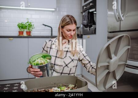 Frau wirft Gemüseschnitzel in einen Komposteimer in der Küche. Stockfoto