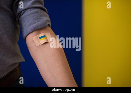 Blutspender mit Verband, nachdem er Blut auf ukrainischem Hintergrund gegeben hat. Stockfoto