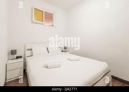 Schlafzimmer mit Kingsize-Bett mit weißem Kopfteil aus Holz, passenden Beistelltischen und zusammengerollten weißen Handtüchern Stockfoto