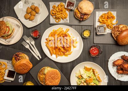 Fastfood-Gerichte mit verschiedenen Hamburgern, Fischkroketten, Chicken Wings, Hähnchen caesar-Salat, Pommes mit Käse und gebratenem Schinken Stockfoto