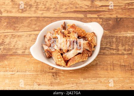 Typische spanische Tapa von Torreznos de soria in Olivenöl gebraten in einer weißen Porzellanschale auf einem alten Holztisch Stockfoto