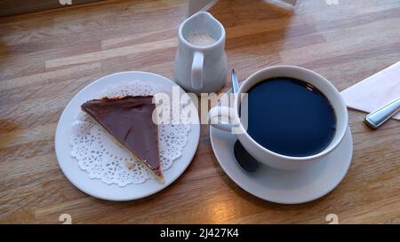 LYTHAM. LANCASHIRE. ENGLAND. 02-27-22. Eine Scheibe mit Schokolade überbacktem Shortbread, serviert mit einer Tasse schwarzen Kaffee und einem kleinen Krug heißer Milch. Stockfoto