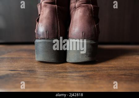 Paar abgenutzte braune Lederschuhe Rückansicht Nahaufnahme Damenschuhe mit abgenutzten dicken schwarzen Gummisohlen stehen auf Holzboden auf dunklem Hintergrund Stockfoto