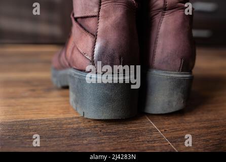 Paar abgenutzte braune Lederschuhe für Frauen Nahaufnahme Damenschuhe mit abgenutzten dicken schwarzen Gummisohlen stehen auf Holzboden im Zimmer mit Möbeln Stockfoto