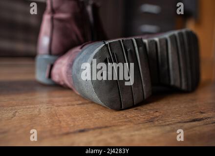 Paar braune Lederschuhe mit beschädigter Sohle Nahaufnahme Damenschuh mit Löchern in dickem Gummi schwarze Sohle lag auf Holzboden in einem Raum Stockfoto