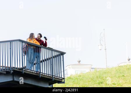 Fröhlicher Reisender, der ein Fernglas hält und seine Freundin am Aussichtspunkt im Freien ansieht Stockfoto