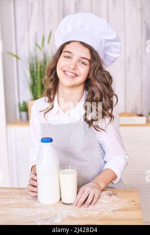 Junges Mädchen, das in der Küche mit Gemüse kocht. Hübsches Kinderportrait. Koch-Student. Attraktive Brünette. Emotionen von Kindern. Menschen, die in Kochschürze backen. Menü Rezept schließen Stockfoto