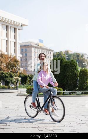 Glücklicher Mann, der tagsüber mit meiner Freundin auf der Stadtstraße Fahrrad fährt Stockfoto