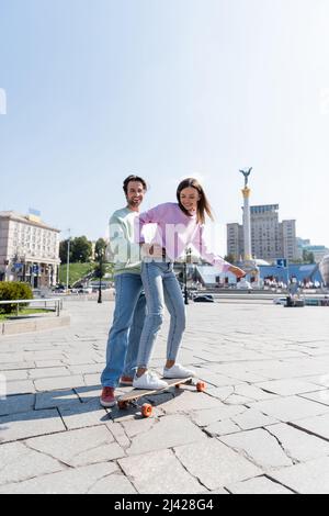 KIEW, UKRAINE - 1. SEPTEMBER 2021: Glücklicher Mann umarmt Freundin auf dem Penny Board auf der Stadtstraße in Kiew Stockfoto