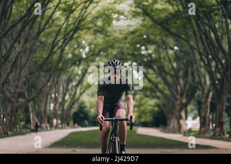 Professioneller Radsportler, der morgens im grünen Sommerpark reiten kann. Sportler mit Sportkleidung, Schutzhelm und Spiegelbrille. Konzept Stockfoto