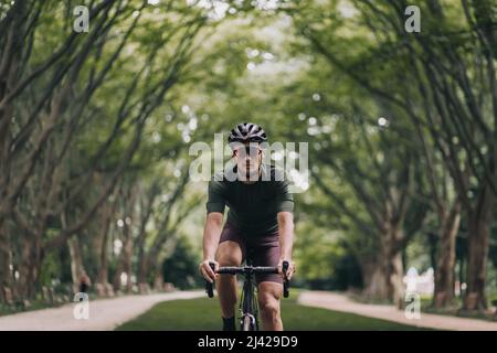 Sportlicher junger Mann mit schwarzem Sportfahrrad für das Radfahren an der frischen Luft. Aktiver Kerl in Helm und Brille mit Outdoor-Training. Regelmäßiges Training für den Aufenthalt Stockfoto