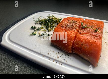 Nahaufnahme von zwei wilden Lachsfilets auf einem weißen Brett mit gemahlenem schwarzem Pfeffer und Thymiangewürz Stockfoto