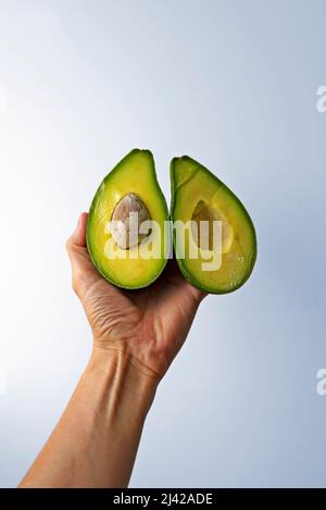 Hälften einer Avocado auf der Hand in einem hellen Hintergrund Stockfoto