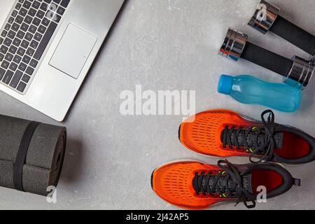 Orangefarbene Sneaker, Hanteln, Wasserflasche, Yogamatte und Laptop auf hellgrauem Betongrund. Das Konzept des Fernsports in Quarantäne. Obere V Stockfoto