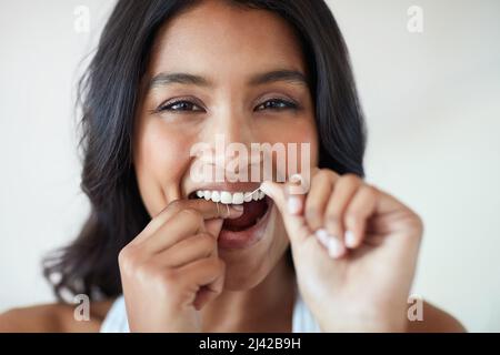 Die Gesundheit meiner Zähne zu einer Priorität zu machen. Porträt einer attraktiven und glücklichen jungen Frau, die ihre Zähne mit Zahnseide putzt. Stockfoto