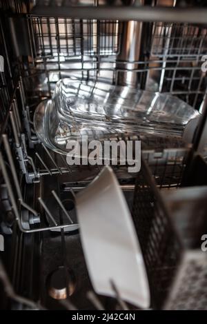 Nahaufnahme der schmutzigen Auflaufform aus Glas auf der unteren Ablage im Geschirrspüler, die mit schmutzigem Geschirr gefüllt ist, schmutziges transparentes, hitzebeständiges Gefäß im Geschirrspüler Stockfoto